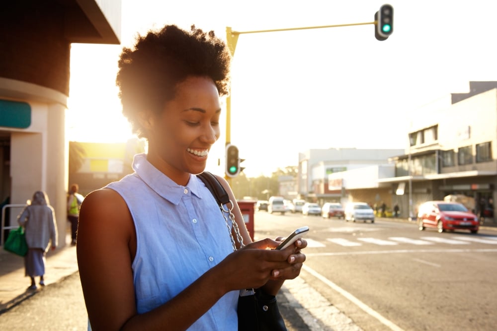 Mulher sorrindo usando smartphone na rua | Como usar a internet móvel a seu favor?