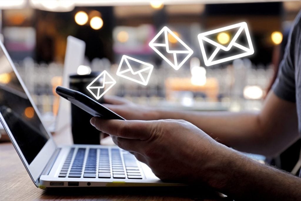 Pessoa com celular na mão sobre o computador| Por que utilizar o E-mail Marketing?
