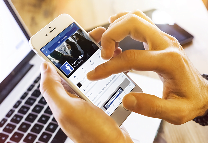 Mãos segurando smartphone acessando Facebook | Você conhece o botão de votação do Facebook?