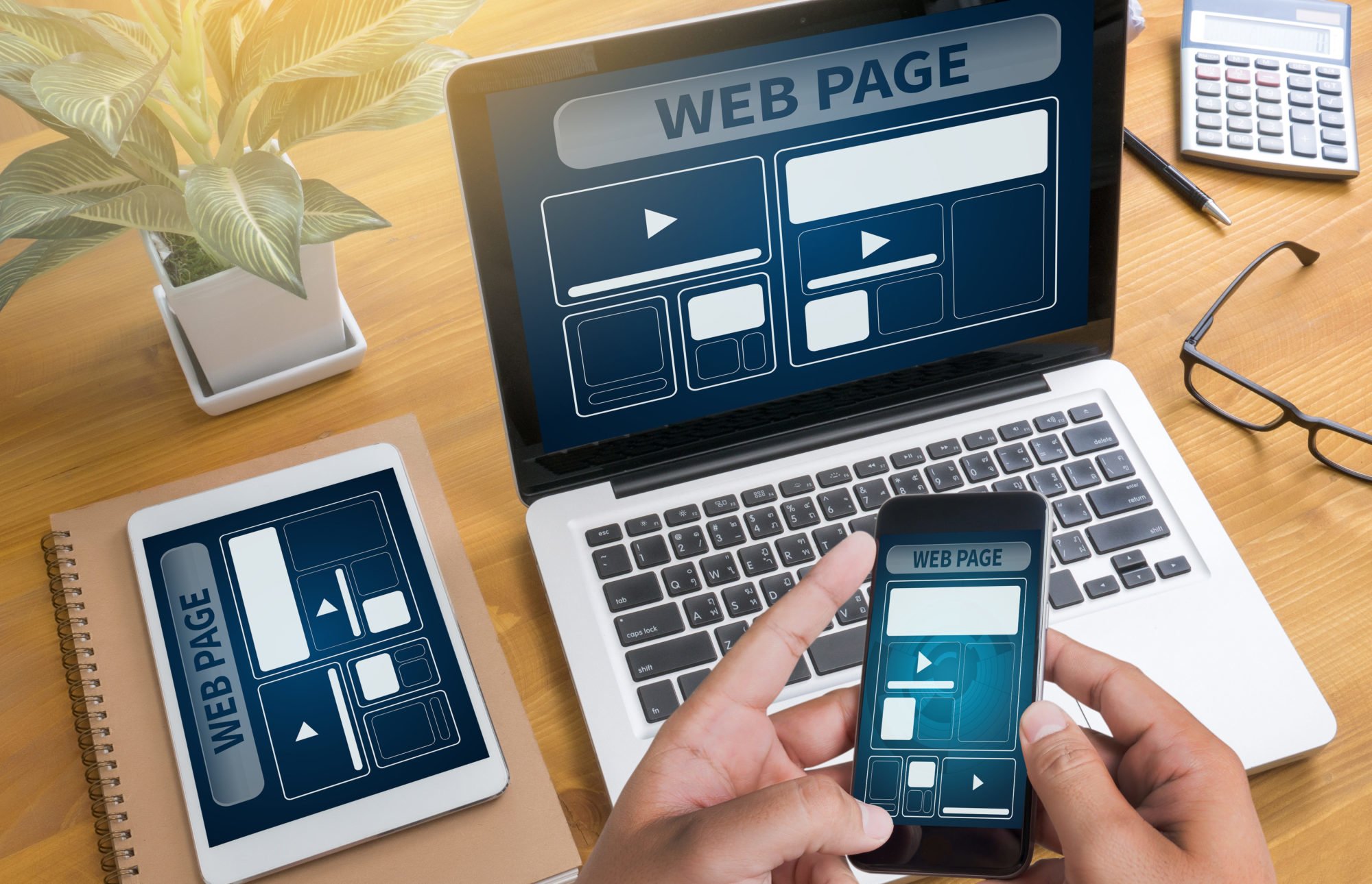 Mesa com caderno, ipod e macbook em cima e mãos segurando iphone